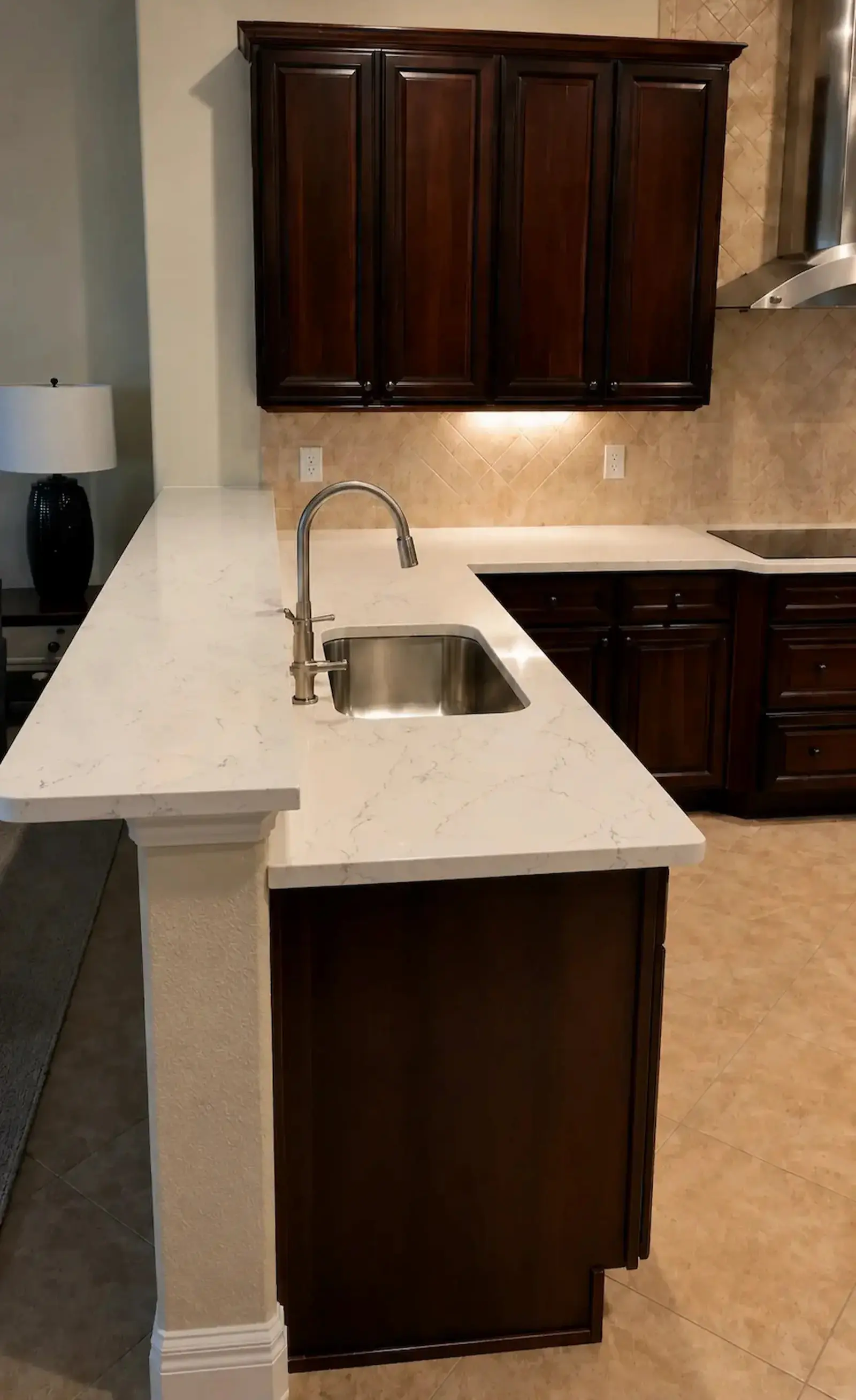 Close-up of a custom kitchen featuring dark wood cabinetry, quartz countertops, and an integrated island sink in Sarasota, Florida